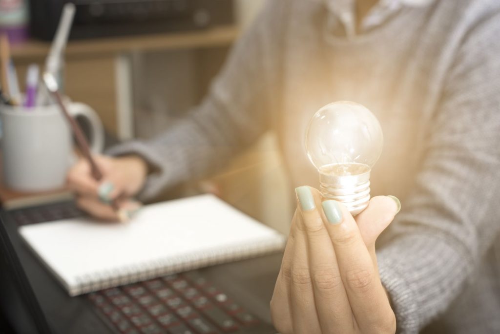 A photo of a person writing notes and holding a lightbulb to signify an idea